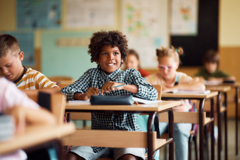 Happy African American elementary student and his classmates having a class at school.